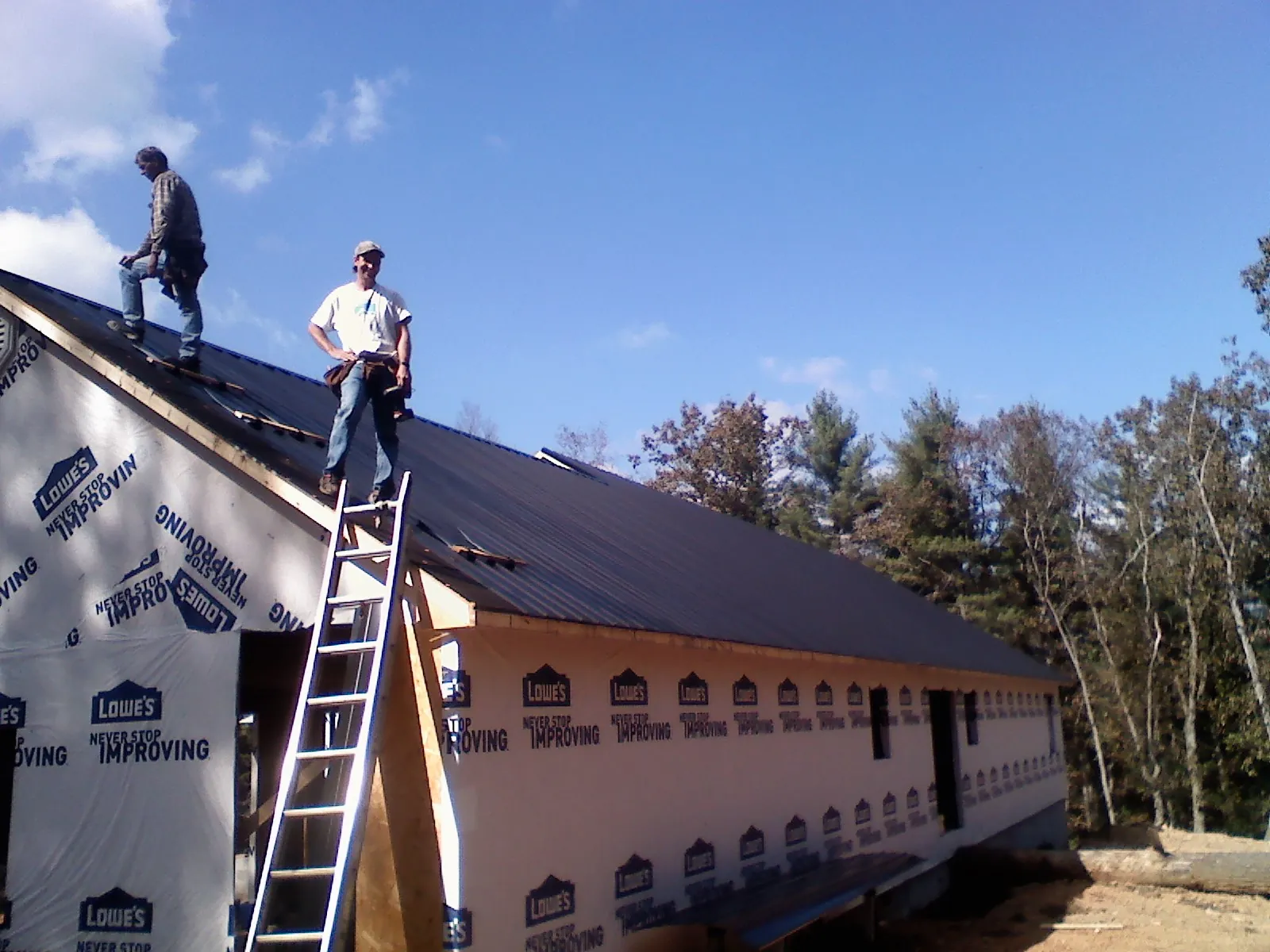 Two roofers standing on a long dark metal roof over a wrapped building in Lowell